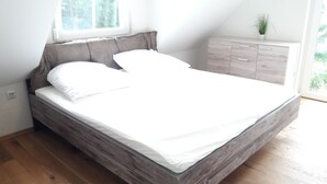 A modern bedroom with a wooden bed frame, white bedding, and a built-in nightstand with drawers. - Vacation home QUELLENHAIN with 5 bedrooms, 2 bathrooms, 3 terraces, garden (Reichshof)