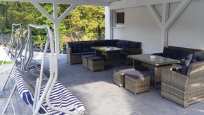 A covered outdoor seating area with wicker furniture and a glass table. - Vacation home QUELLENHAIN with 5 bedrooms, 2 bathrooms, 3 terraces, garden (Reichshof)