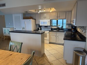 A kitchen with white cabinets, a black countertop, a stainless steel trash can, and a view to the outside. - Beachfront 2/2 condo, 2 King Master Suites, 2 Balconies, Just Updated (South Padre Island)