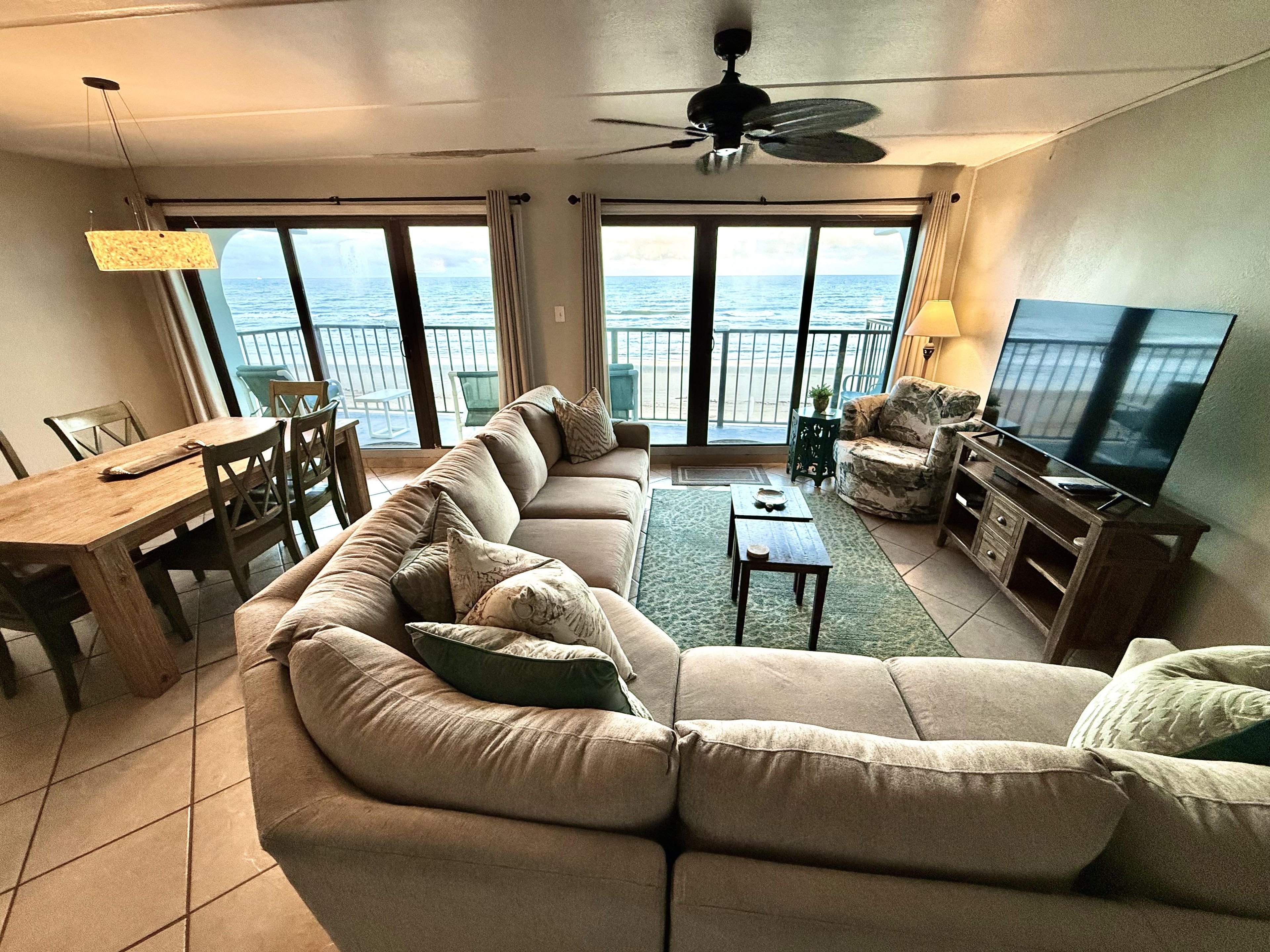 Una sala de estar con un sofá grande, una televisión y un balcón con vistas al mar.