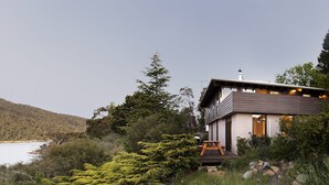 Una casa moderna con terraza, rodeada de árboles y un lago.