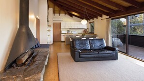 Una sala de estar moderna con chimenea de piedra, un sofá de cuero y un comedor con cocina al fondo.