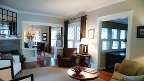 A spacious living room with a fireplace, a dining area, and a view of the outdoors through large windows. - Beautiful Historic Old Northend Bungalow with amazing outdoor space (Colorado Springs)