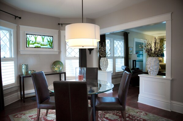Un comedor con mesa de vidrio, sillas de cuero, una lámpara colgante grande, un ventanal con vitrales y jarrones decorativos.