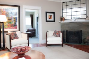 A living room with two white armchairs, a fireplace, a framed picture, and a bowl of decorative eggs on a table.