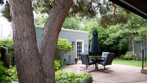 A patio area with a table and chairs, surrounded by greenery and a tree. - Beautiful Historic Old Northend Bungalow with amazing outdoor space (Colorado Springs)