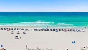 Une plage bordée de rangées de parasols et de chaises longues, un ciel dégagé et l’océan.