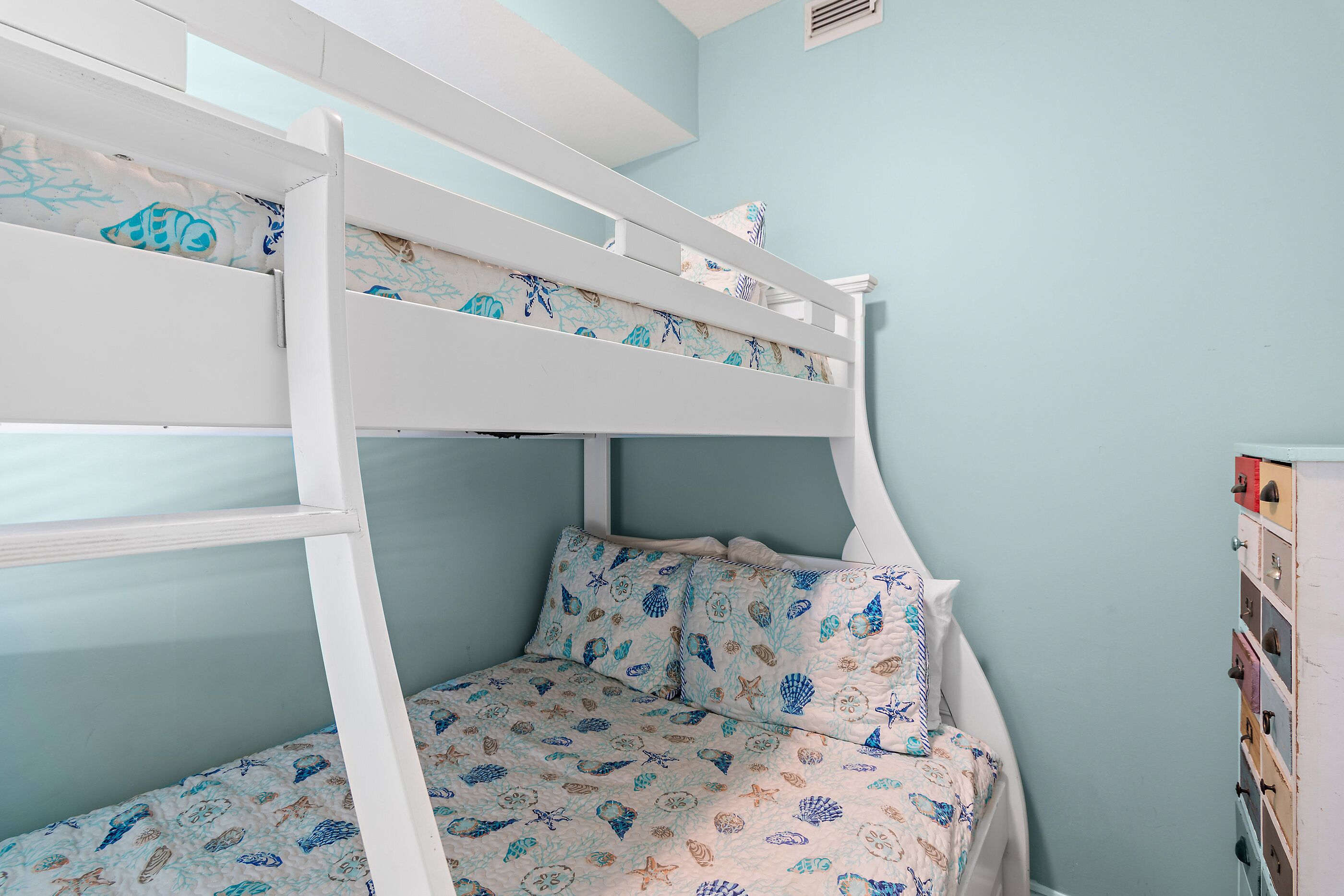 Un lit superposé avec une couvre-lit à motifs, une tête de lit blanche et une bibliothèque intégrée.