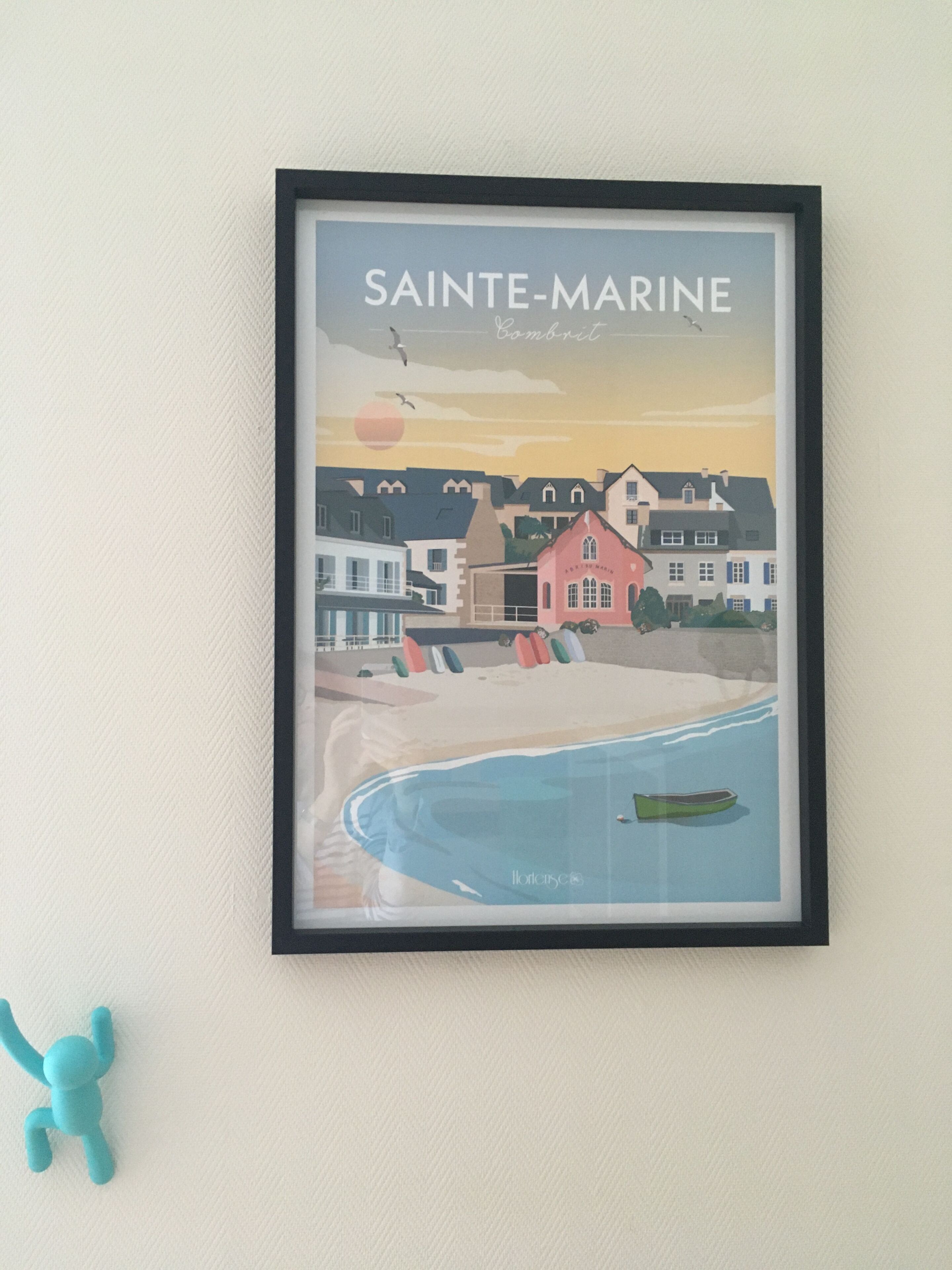 Une œuvre d’art encadrée représentant Sainte-Marine, avec une scène de plage, un bateau et des bâtiments.