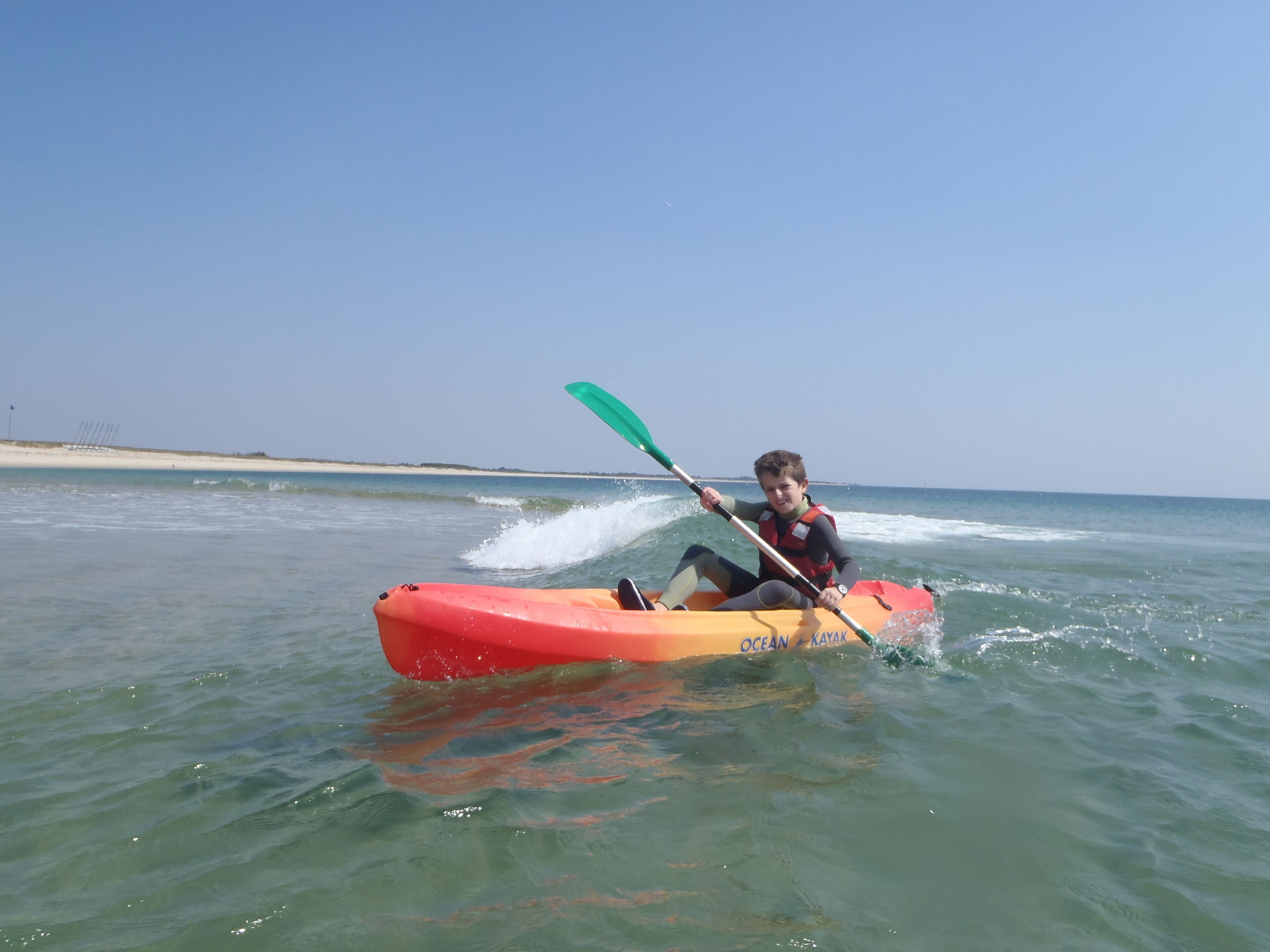 A person in a red kayak on calm water with a clear sky and a distant shoreline.