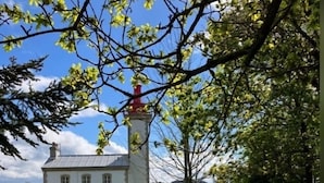 Een wit gebouw met een rode toren, omgeven door een stenen muur en een pad dat naar een waterpartij leidt.
