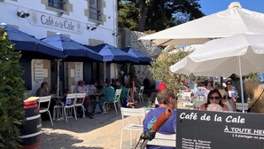 Een terras met tafels en parasols, omringd door bomen en een stenen muur.