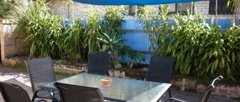An outdoor patio area with a table and chairs under a blue shade.