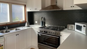 A modern kitchen with white cabinetry, a black brick backsplash, a stainless steel stove, and an oven. - the whitehouse Port fairy in  the heart of town,  pet friendly (Port Fairy)