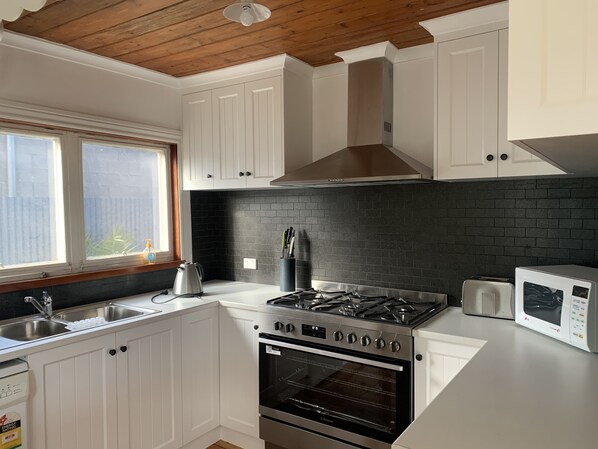 A modern kitchen with white cabinetry, a black brick backsplash, a stainless steel stove, and an oven.