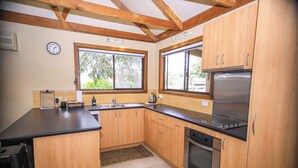 Una cocina con gabinetes de madera, encimera negra, refrigerador de acero inoxidable y ventana con vista a la vegetación.