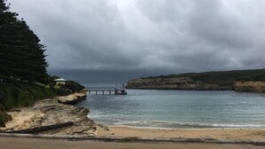 Escena costera con una playa arenosa, una zona cubierta de hierba y un acantilado rocoso.