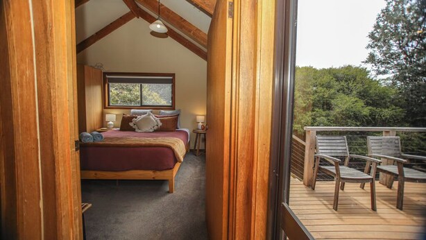 Un dormitorio con cama de madera, una ventana y un balcón con sillas.