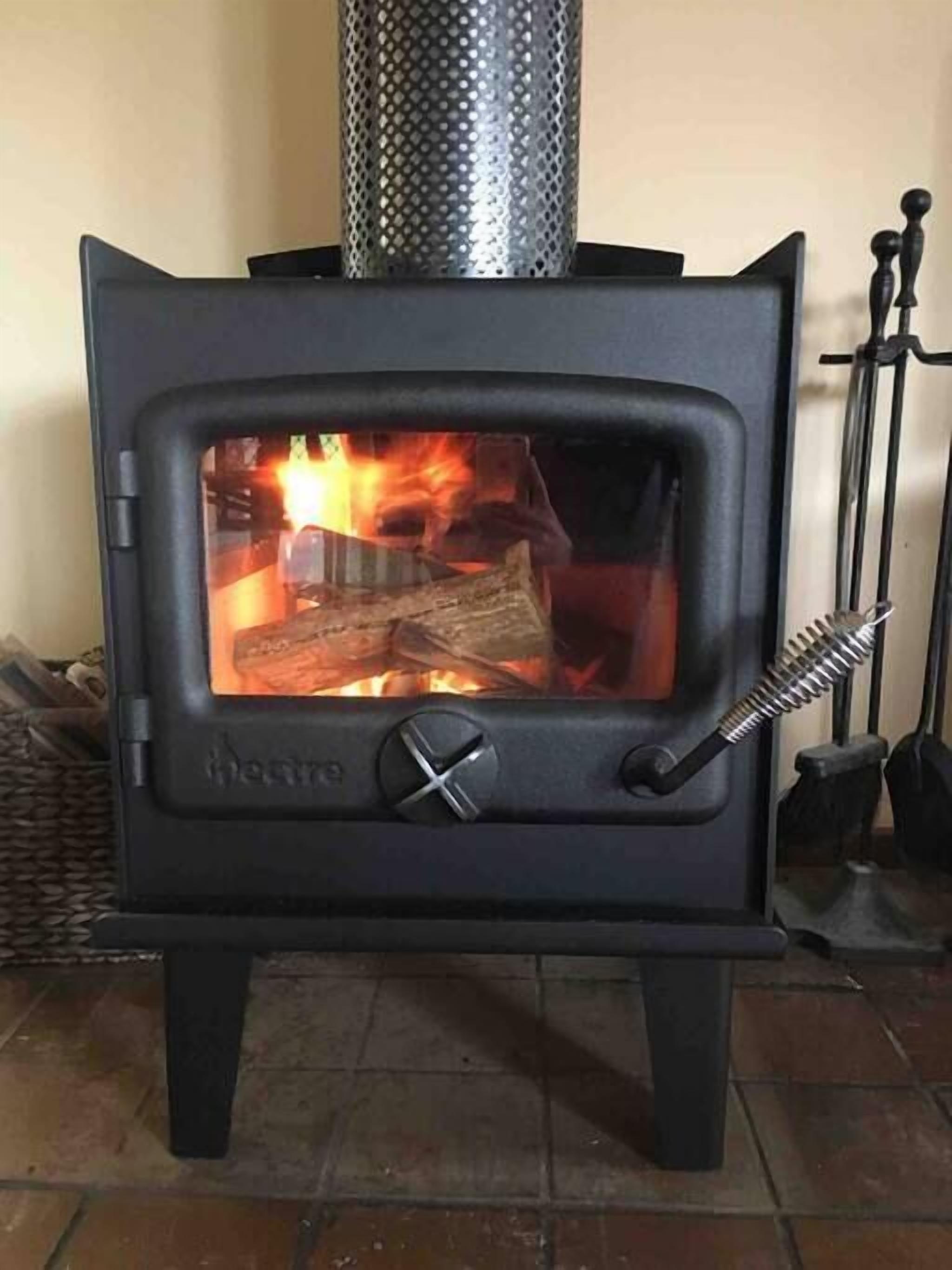 Un poêle à bois avec une cheminée en métal, un feu qui brûle à l'intérieur et un bouton de réglage.