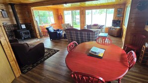 A cozy cabin interior with a central red table, a fireplace, and a TV.