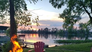 A campfire with chairs and a dock by a lake at sunset.