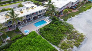 Eine Luftaufnahme eines Hotels direkt am Strand mit einem Schwimmbad, mehreren Balkonen und üppiger Vegetation.