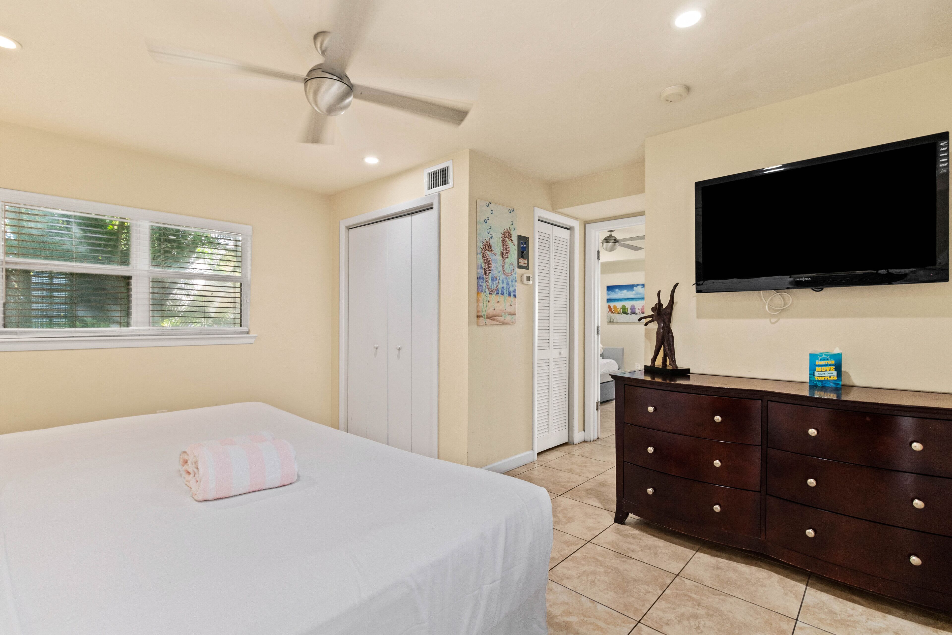 A bedroom with a bed, a ceiling fan, a TV, a dresser, and a window with blinds.