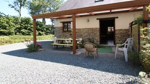 A covered patio area with a stone wall, wooden furniture, and a gravel driveway. - Quiet house near Saint-Lô with fireplace and garden (Bourgvallées)