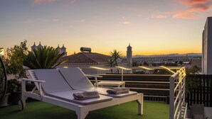A rooftop terrace with a white lounge chair, a small table, and string lights.