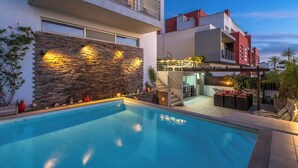 A modern poolside area with a stone wall, outdoor seating, and a staircase leading to an upper level.