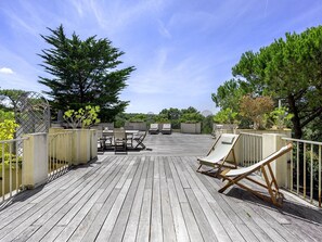 Eine Holzterrasse mit Gartenmöbeln, darunter ein Tisch, Stühle und eine Liege.