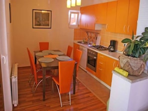 A compact kitchen with orange cabinets, a dining table with chairs, and a small oven.