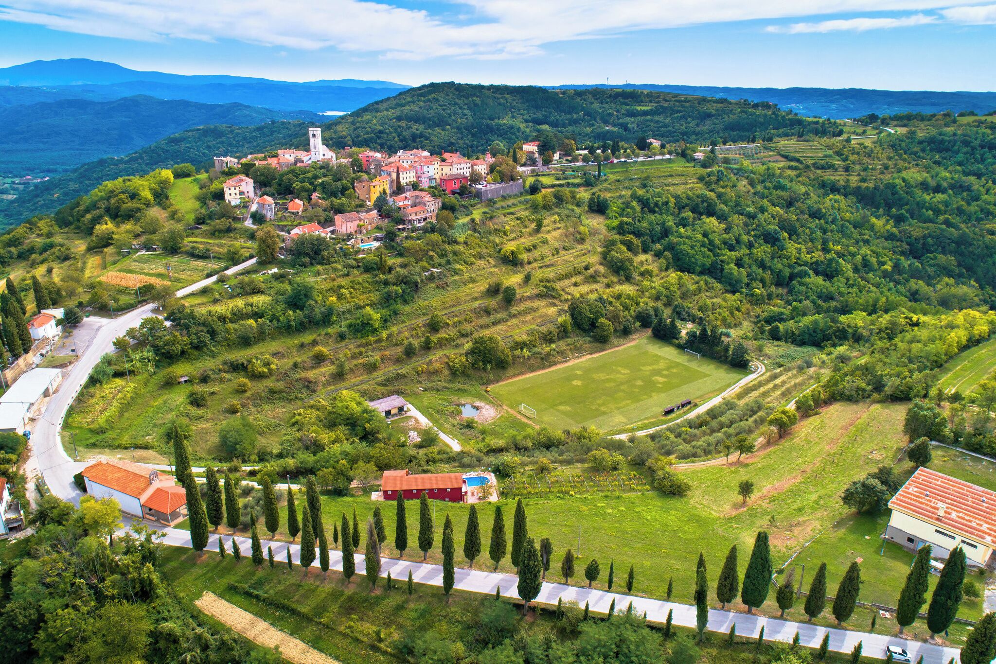 An aerial view of a town with a prominent church, terraced fields, and a winding road.