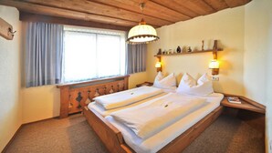 Een slaapkamer met een houten bed, twee nachtkastjes, een wandplank met decoratieve spullen en een raam met gordijnen.
