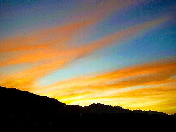 A mountain range silhouette against a sunset sky with vibrant orange and yellow hues. - Penthouse views from every window...overlooking entire city and mountain ranges (Colorado Springs)