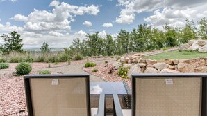Un área de estar al aire libre con una mesa y sillas, rodeada por un jardín ajardinado con rocas y plantas, bajo un cielo parcialmente nublado.