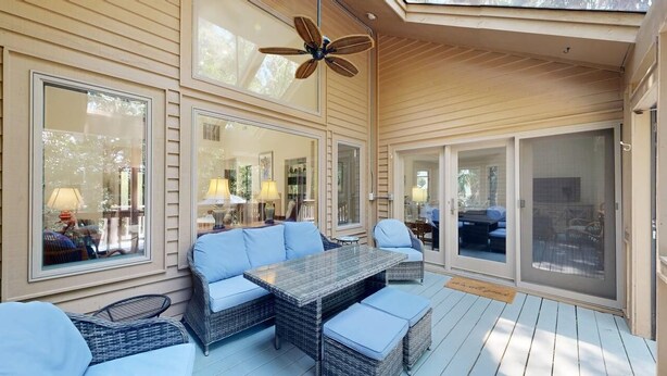 A covered patio with wicker furniture, large windows, and a ceiling fan. - Comfortable Palmetto Dunes Home with Private Pool and Screened in Porch (Hilton Head)