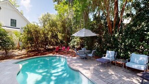 A backyard with a swimming pool, patio furniture, and a large umbrella. - Comfortable Palmetto Dunes Home with Private Pool and Screened in Porch (Hilton Head)