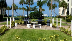 A patio area with two barbecue grills, white stone benches, and palm trees. - Island House Beach Resort V33 (Siesta Key)