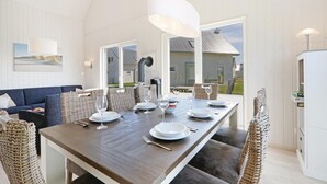 Un espace repas avec une longue table, des chaises en osier et de la vaisselle blanche.