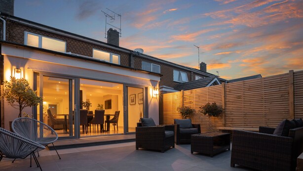 Un patio moderno con mobiliario exterior, un ventanal que da a un comedor y una cerca de madera.