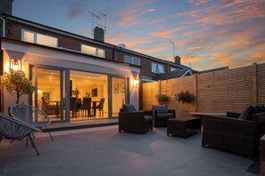 A modern patio with outdoor furniture, a glass door leading to a dining area, and a wooden fence. - Modern Living in Old Town Stratford-upon-Avon (Stratford-upon-Avon)