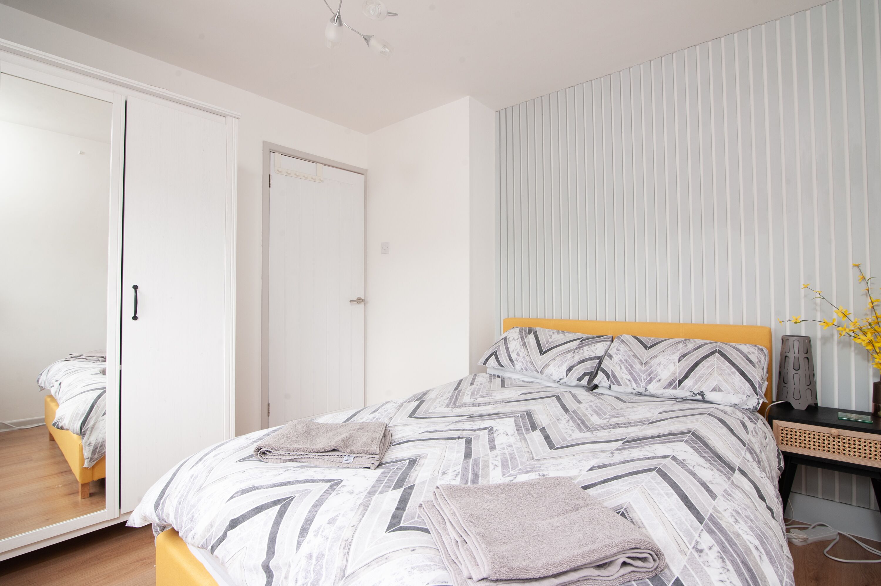 A bedroom with a bed, a wardrobe, a bedside table, and a mirror.