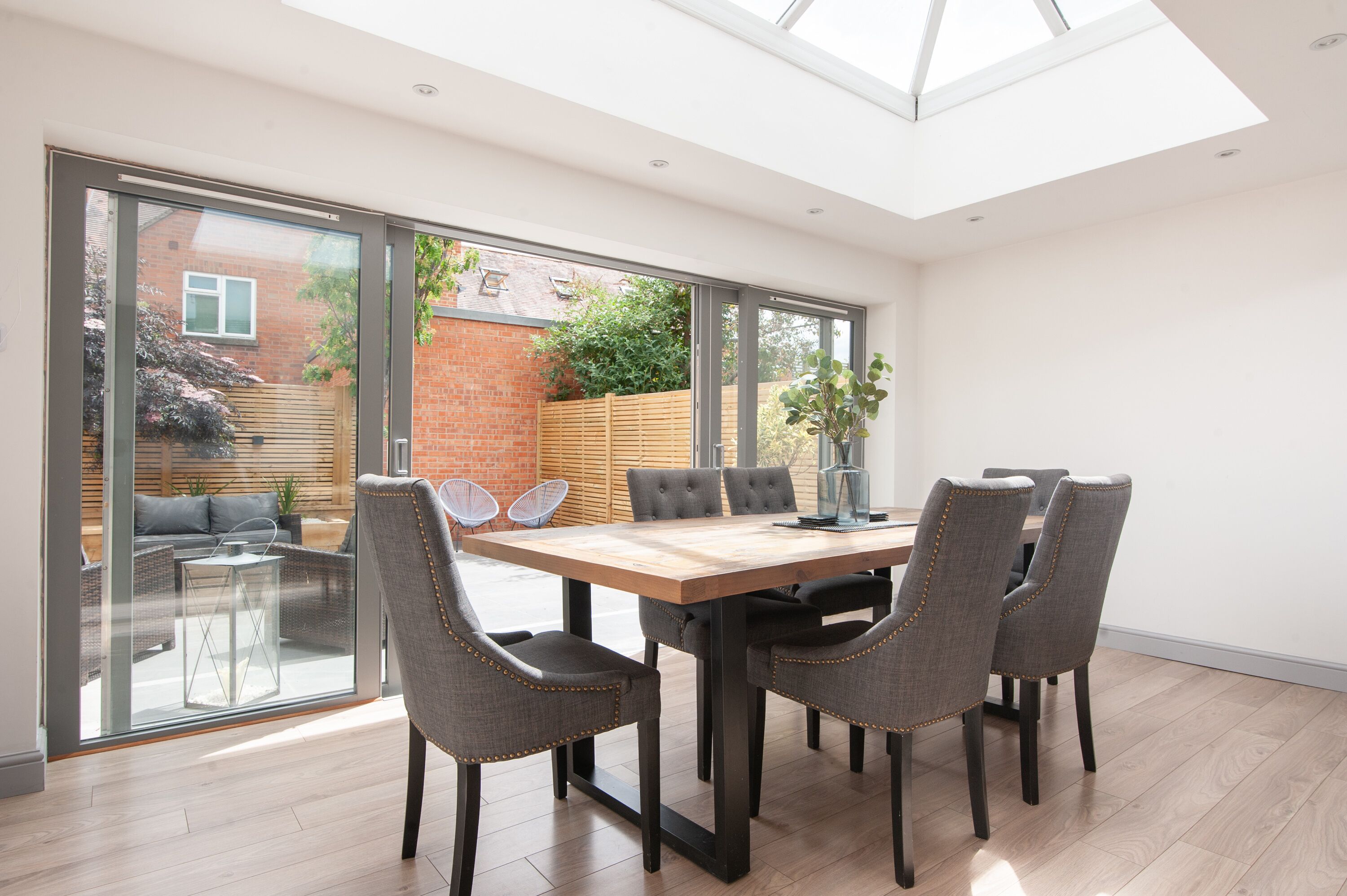 A modern dining area with a large table and six chairs, a glass door leading to a patio, and a skylight above.