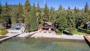 A lakeside property with a dock, boats, and a large house surrounded by trees. - Lake Front Retreat With Your Private Beach & Hot Tub  (Tahoe Vista)