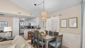 Une cuisine moderne avec des meubles blancs, un coin repas doté d’une table et de chaises en bois, et un luminaire suspendu.