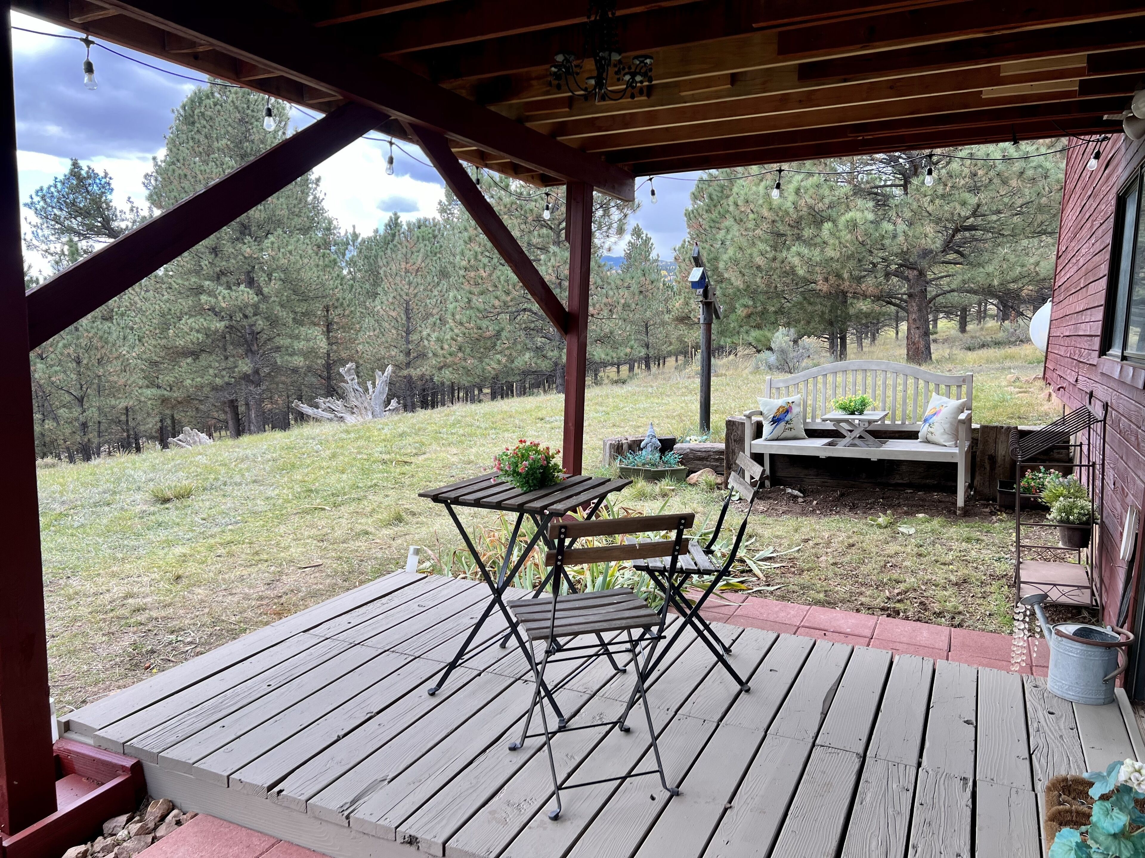 Une terrasse en bois avec une table et des chaises, un banc et un pot de fleurs.