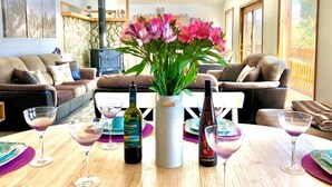 Una sala de estar con chimenea, una mesa con copas de vino y un florero con flores.