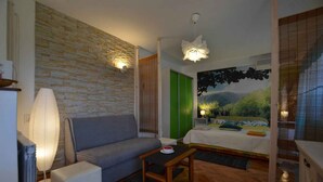 A room with a stone wall, a bed with a green accent wall, a sofa, a table, and a lamp. - Studio with balcony and air conditioning (Rovinj)