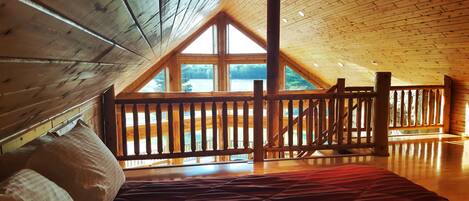 A bedroom with a wooden ceiling, a large window, and a view of a lake.